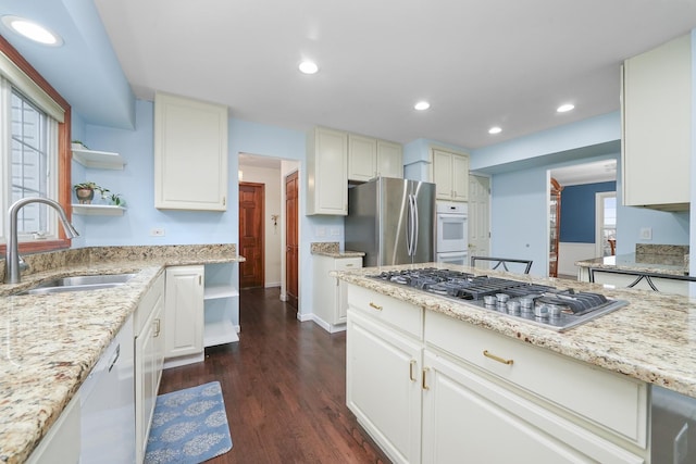 kitchen featuring appliances with stainless steel finishes, sink, white cabinets, dark hardwood / wood-style flooring, and light stone counters