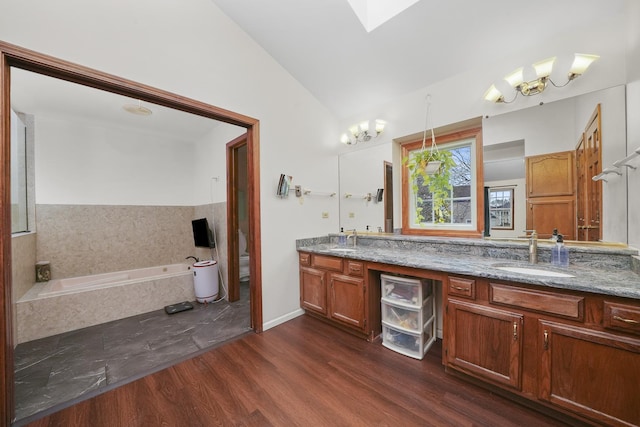 bathroom with wood-type flooring, lofted ceiling, vanity, toilet, and tiled tub