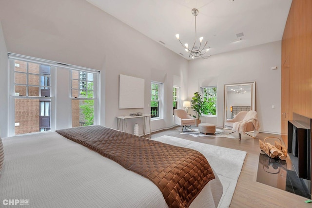 bedroom with a towering ceiling, a chandelier, multiple windows, and light wood-type flooring