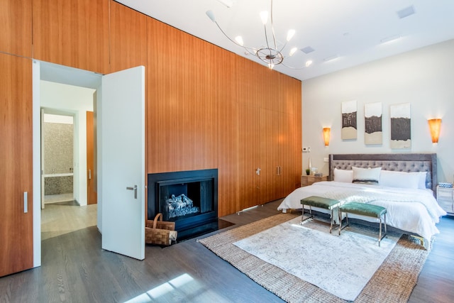 bedroom with wooden walls, a large fireplace, dark hardwood / wood-style flooring, a closet, and a chandelier