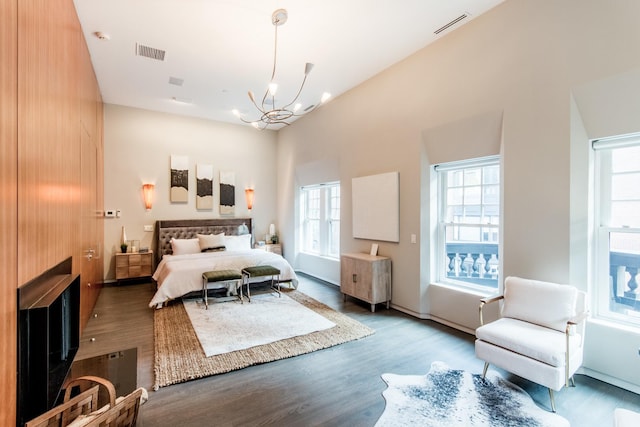 bedroom with a high ceiling, hardwood / wood-style floors, a notable chandelier, and a fireplace