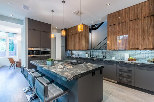 kitchen with a breakfast bar, appliances with stainless steel finishes, dark stone countertops, a kitchen island, and decorative light fixtures