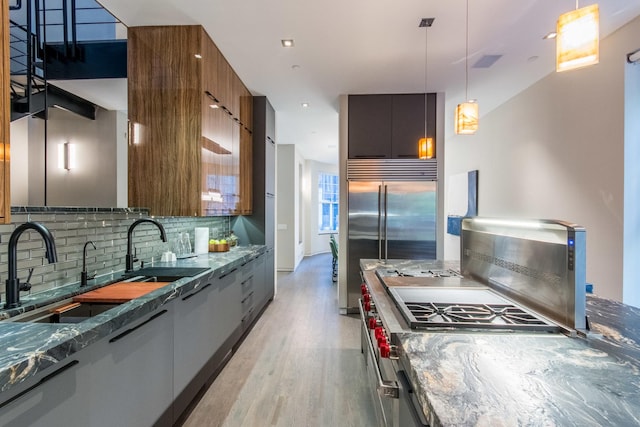 kitchen with backsplash, sink, hanging light fixtures, and dark stone countertops