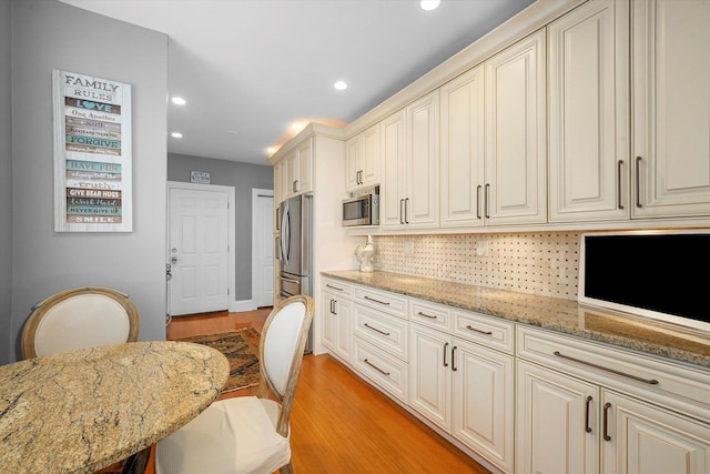 kitchen featuring a kitchen bar, light hardwood / wood-style flooring, appliances with stainless steel finishes, light stone countertops, and backsplash