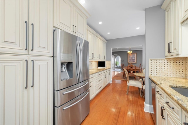 kitchen featuring decorative light fixtures, light hardwood / wood-style flooring, appliances with stainless steel finishes, light stone countertops, and decorative backsplash