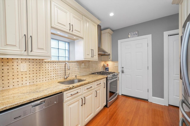 kitchen with light stone counters, sink, stainless steel appliances, and wall chimney exhaust hood