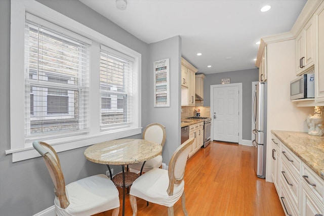 kitchen featuring appliances with stainless steel finishes, light stone counters, tasteful backsplash, light hardwood / wood-style floors, and cream cabinetry