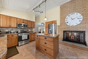 kitchen featuring appliances with stainless steel finishes, tasteful backsplash, a fireplace, a kitchen island, and decorative light fixtures