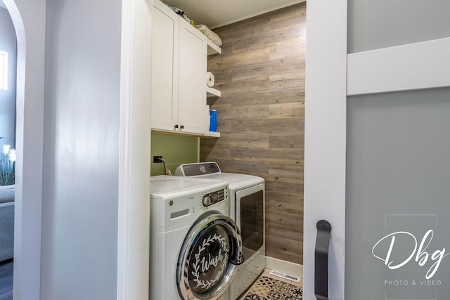 washroom with arched walkways, washing machine and dryer, cabinet space, and wooden walls