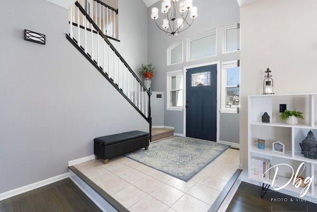 foyer entrance featuring a notable chandelier, a towering ceiling, wood finished floors, baseboards, and stairs