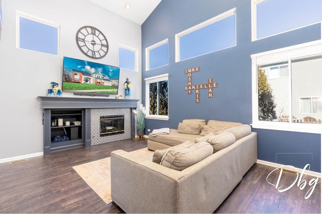 living area with a tiled fireplace, wood finished floors, a towering ceiling, and baseboards