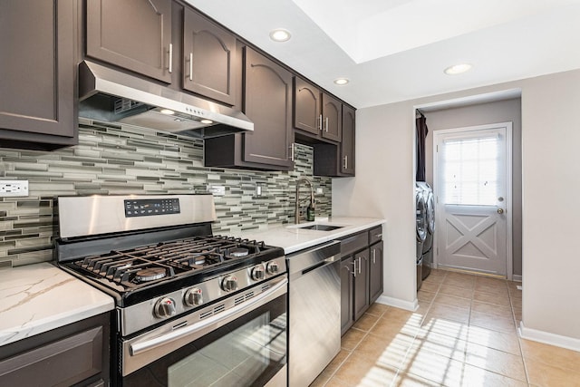 kitchen featuring appliances with stainless steel finishes, washer and dryer, sink, light stone counters, and dark brown cabinetry