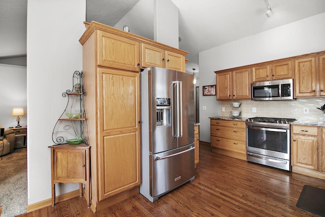 kitchen featuring appliances with stainless steel finishes, dark hardwood / wood-style floors, tasteful backsplash, light stone countertops, and vaulted ceiling