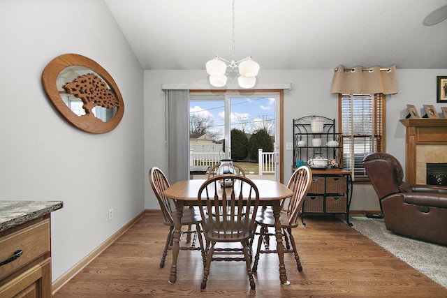 dining room featuring a tiled fireplace, a wealth of natural light, light hardwood / wood-style floors, and a chandelier