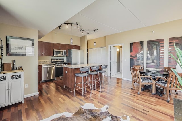 kitchen featuring a breakfast bar, a center island, dark brown cabinets, appliances with stainless steel finishes, and hardwood / wood-style flooring