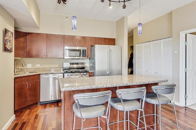 kitchen with sink, stainless steel appliances, a center island, wood-type flooring, and decorative light fixtures