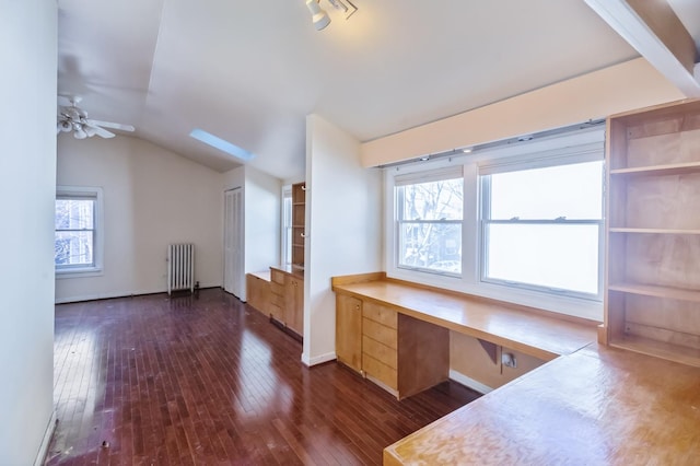 unfurnished office featuring lofted ceiling, dark wood-type flooring, radiator heating unit, built in desk, and a healthy amount of sunlight