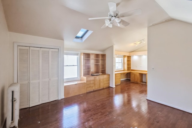 interior space with dark hardwood / wood-style floors, vaulted ceiling with skylight, radiator, ceiling fan, and a closet