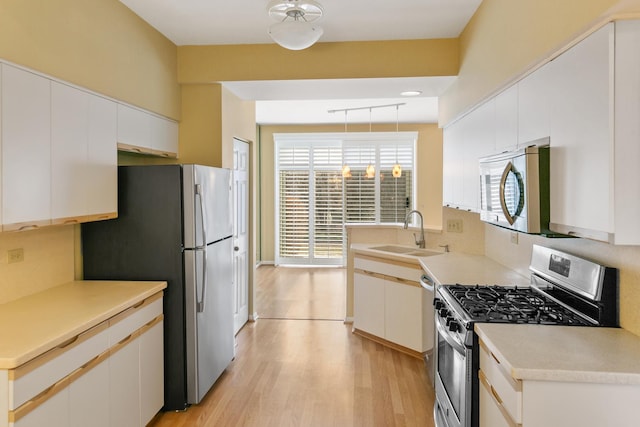 kitchen with sink, white cabinetry, decorative light fixtures, light hardwood / wood-style flooring, and stainless steel appliances