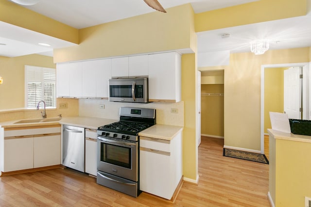 kitchen featuring appliances with stainless steel finishes, tasteful backsplash, sink, white cabinets, and light hardwood / wood-style floors