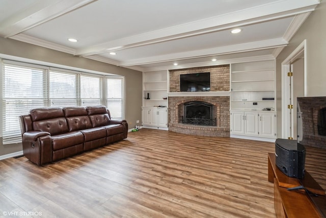 living room featuring built in features, ornamental molding, a brick fireplace, beamed ceiling, and light wood-type flooring