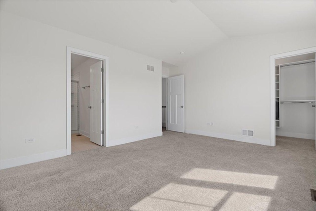 unfurnished bedroom featuring vaulted ceiling, a walk in closet, light carpet, and a closet