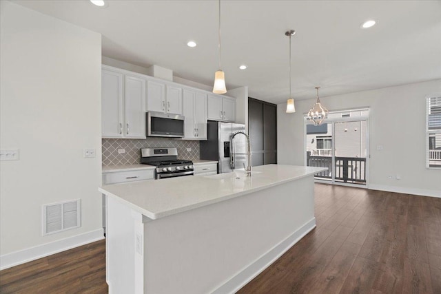 kitchen featuring pendant lighting, appliances with stainless steel finishes, white cabinetry, tasteful backsplash, and a center island with sink