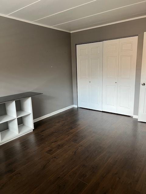 unfurnished bedroom with crown molding, dark wood-type flooring, and a closet