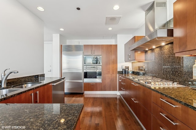 kitchen featuring sink, dark wood-type flooring, dark stone countertops, built in appliances, and island range hood