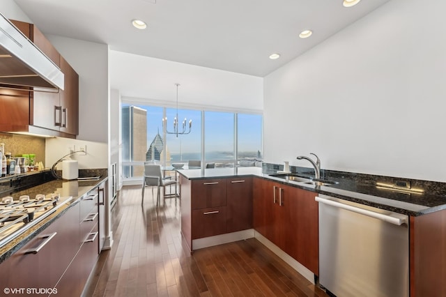 kitchen with sink, dark stone countertops, stainless steel dishwasher, pendant lighting, and range hood