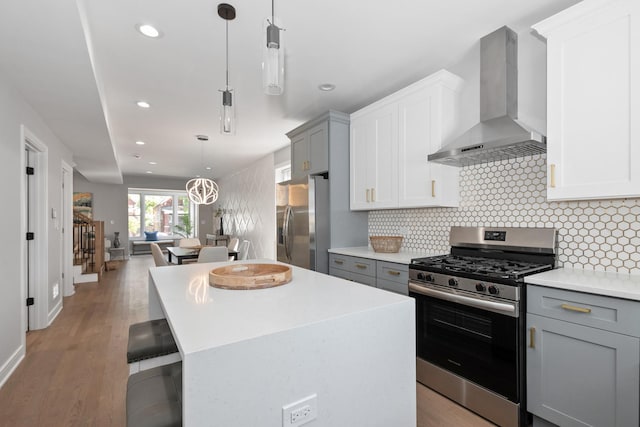 kitchen with wall chimney range hood, appliances with stainless steel finishes, gray cabinetry, a center island, and decorative light fixtures