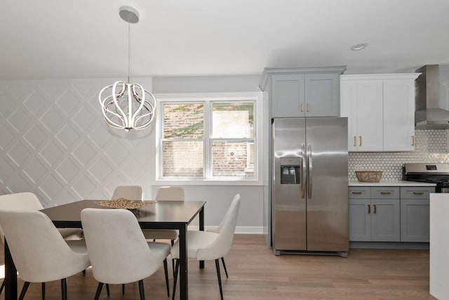 kitchen with gray cabinetry, hanging light fixtures, stainless steel appliances, tasteful backsplash, and wall chimney exhaust hood