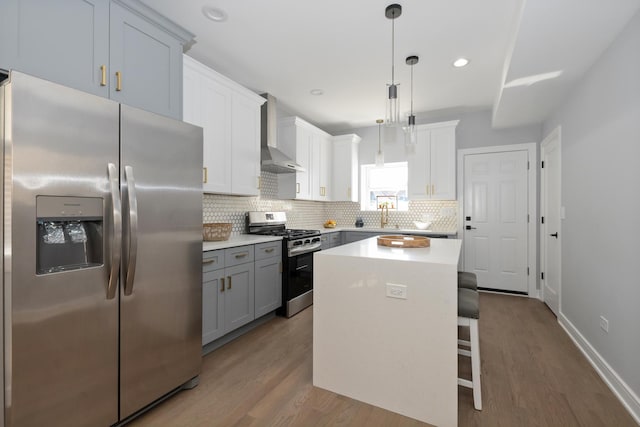 kitchen featuring a breakfast bar, hanging light fixtures, a center island, stainless steel appliances, and wall chimney exhaust hood