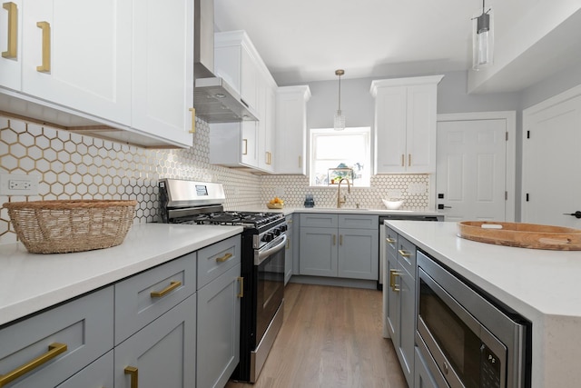 kitchen featuring pendant lighting, sink, gray cabinetry, stainless steel appliances, and wall chimney exhaust hood