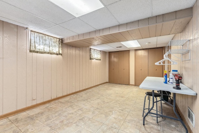 basement featuring wood walls, a drop ceiling, visible vents, and tile patterned floors