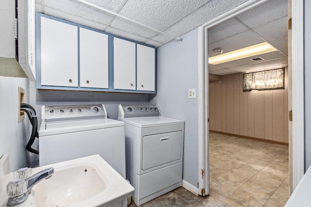 washroom with wood walls, a sink, visible vents, baseboards, and washing machine and clothes dryer