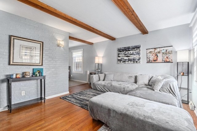 living room featuring brick wall, wood finished floors, beam ceiling, and baseboards