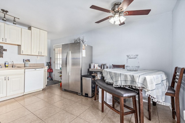 kitchen featuring light tile patterned floors, light countertops, freestanding refrigerator, white dishwasher, and a sink