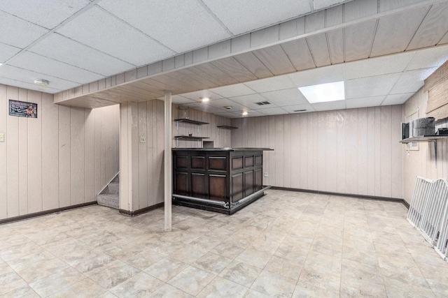 finished below grade area with a bar, stairway, a drop ceiling, and baseboards