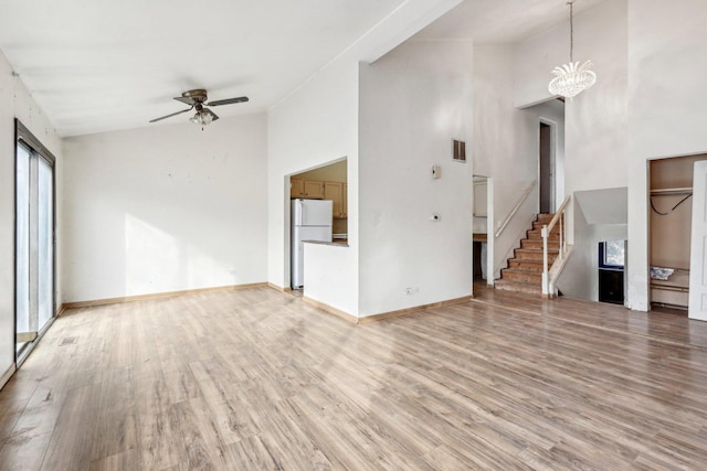 unfurnished living room with hardwood / wood-style floors, ceiling fan with notable chandelier, and high vaulted ceiling