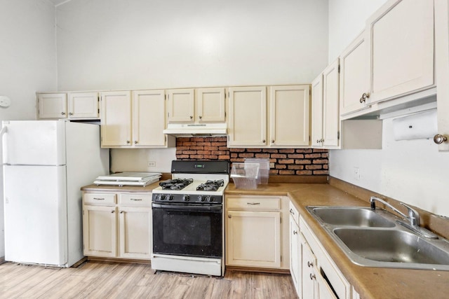 kitchen featuring sink, range with gas stovetop, white fridge, a towering ceiling, and light hardwood / wood-style floors