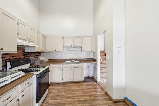 kitchen featuring a towering ceiling, sink, range with gas cooktop, and white cabinets