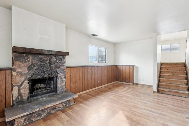 unfurnished living room with a fireplace, wood walls, and light wood-type flooring