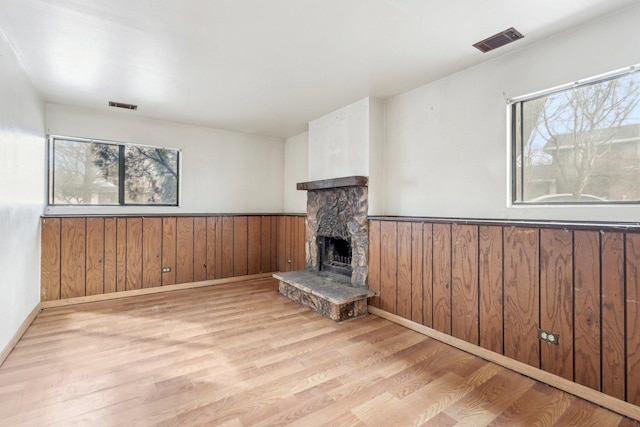 unfurnished living room featuring wooden walls, a stone fireplace, and light wood-type flooring