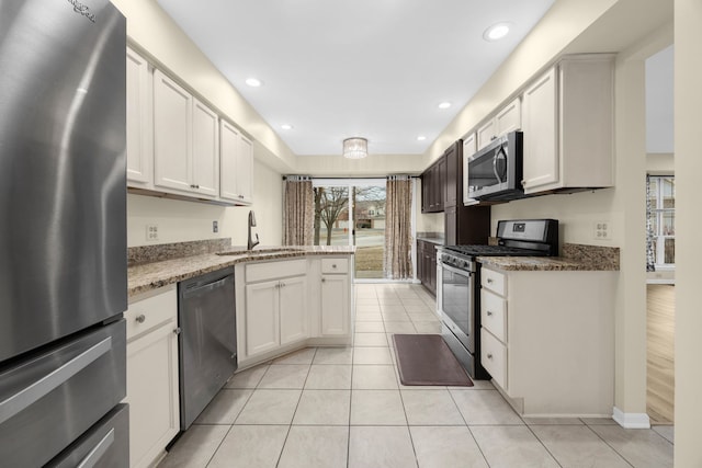 kitchen featuring light tile patterned floors, appliances with stainless steel finishes, white cabinets, a sink, and a peninsula