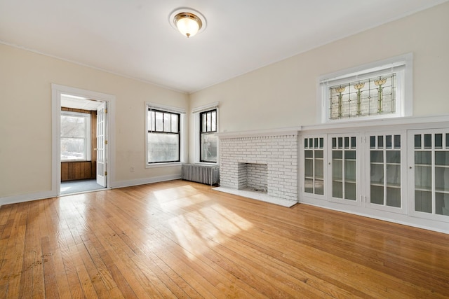 unfurnished living room with radiator heating unit, a fireplace, and light hardwood / wood-style flooring