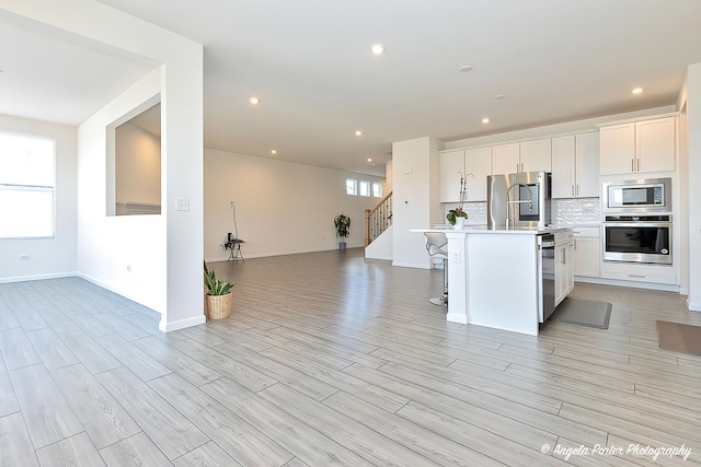 kitchen with appliances with stainless steel finishes, a kitchen island with sink, backsplash, a kitchen breakfast bar, and white cabinets