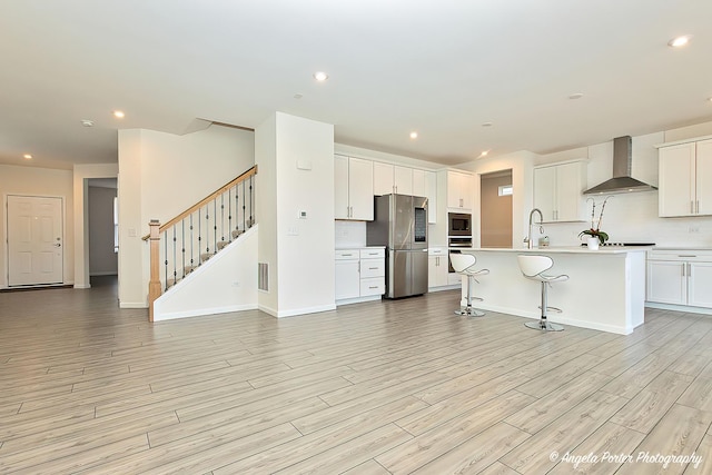 kitchen with a kitchen island with sink, white cabinetry, wall chimney exhaust hood, and appliances with stainless steel finishes