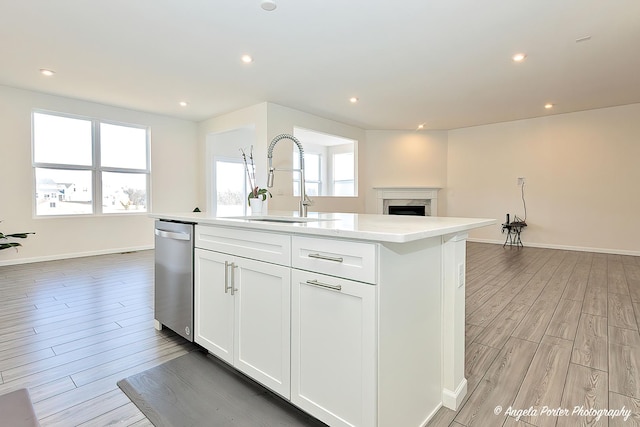 kitchen featuring sink, dishwasher, light hardwood / wood-style floors, an island with sink, and white cabinets