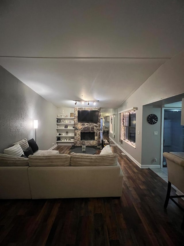 living room with rail lighting, a stone fireplace, dark wood-type flooring, and lofted ceiling